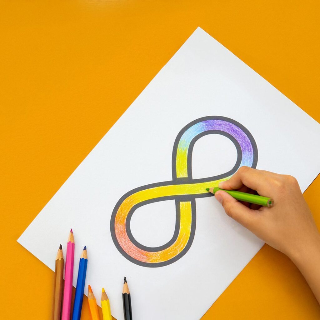 A hand coloring a rainbow infinity symbol with colored pencils on white paper